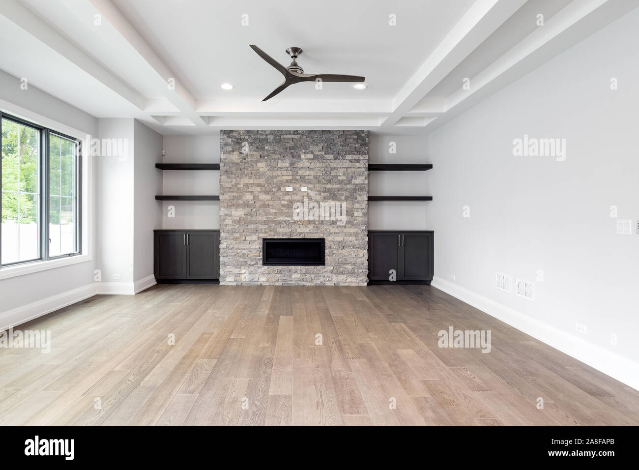 Un moderne, mis à jour le vide d'une salle de séjour avec parquet, une cheminée en brique entouré d'étagères et armoires, et une cour arrière. Banque D'Images