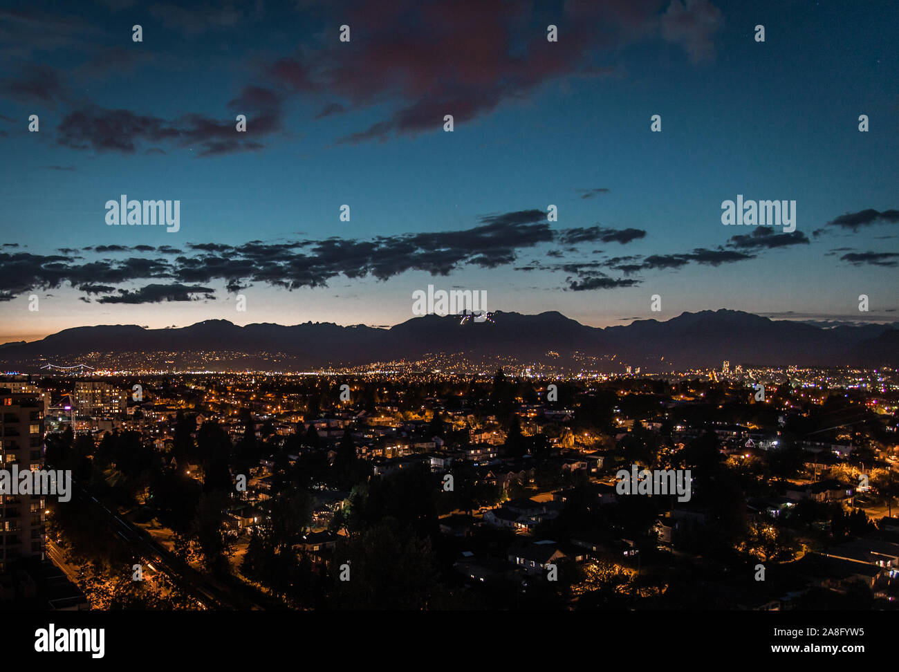 Les lumières de la ville de Vancouver avec des montagnes de l'Est à la tombée du fond avec derniers rayons du coucher de soleil en été et de Grouse Mountain lumières ski Banque D'Images