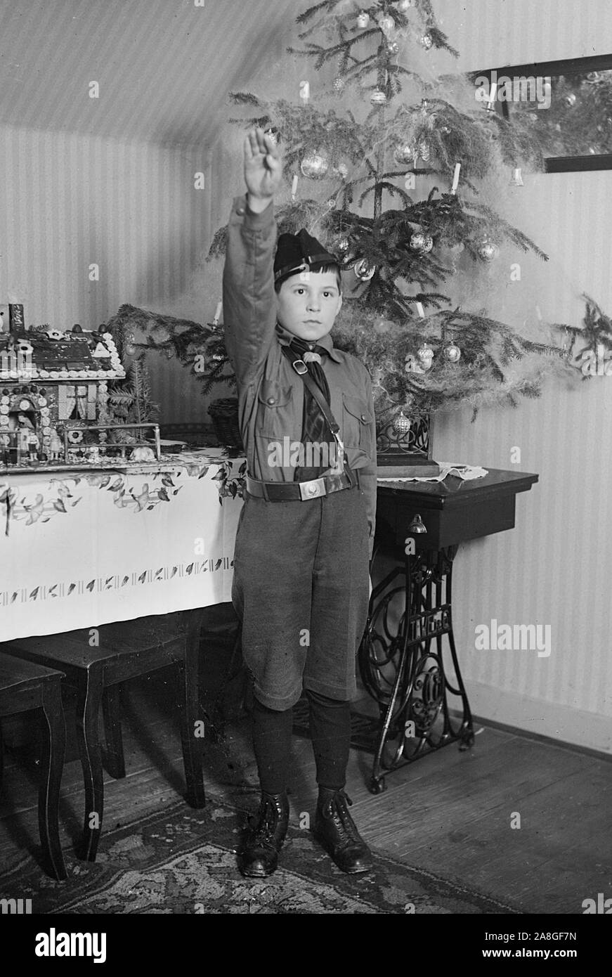 Un des membres de la jeunesse hitlérienne est avec un salut nazi devant l'arbre de Noël dans l'Allemagne des années 1930. Banque D'Images