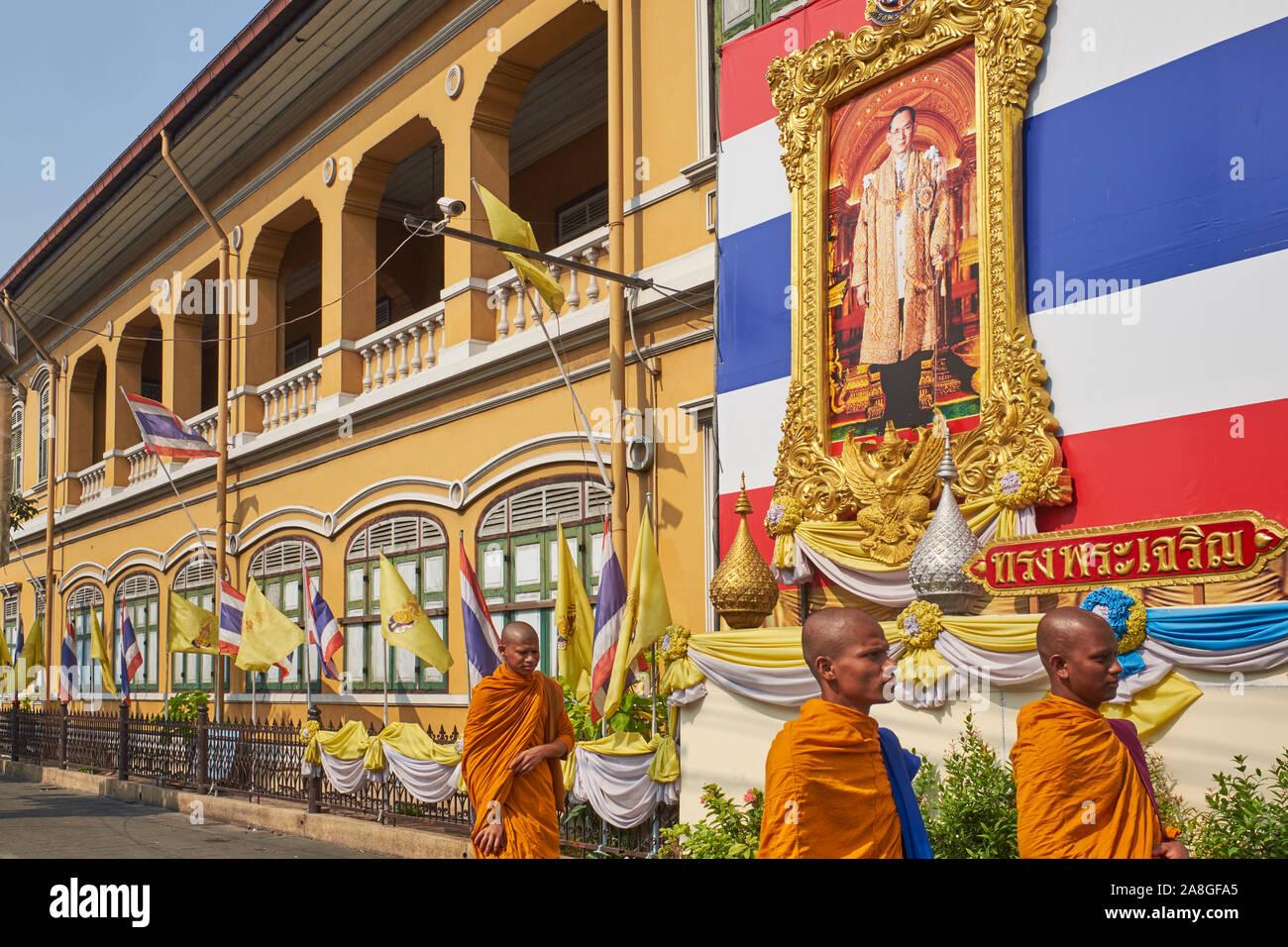 Les moines bouddhistes du Sri Lanka passez sous un portrait du roi Bhumipol Thaï en retard et un grand drapeau à Suan thaï ; École Kularb, Bangkok, Thaïlande Banque D'Images