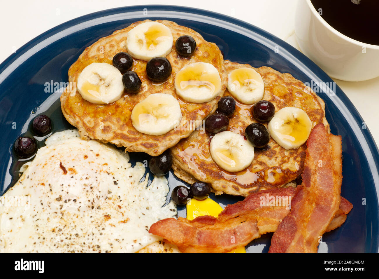 Assiette petit-déjeuner de crêpes aux bananes et aux bleuets, les œufs au plus facile, et du bacon. Banque D'Images