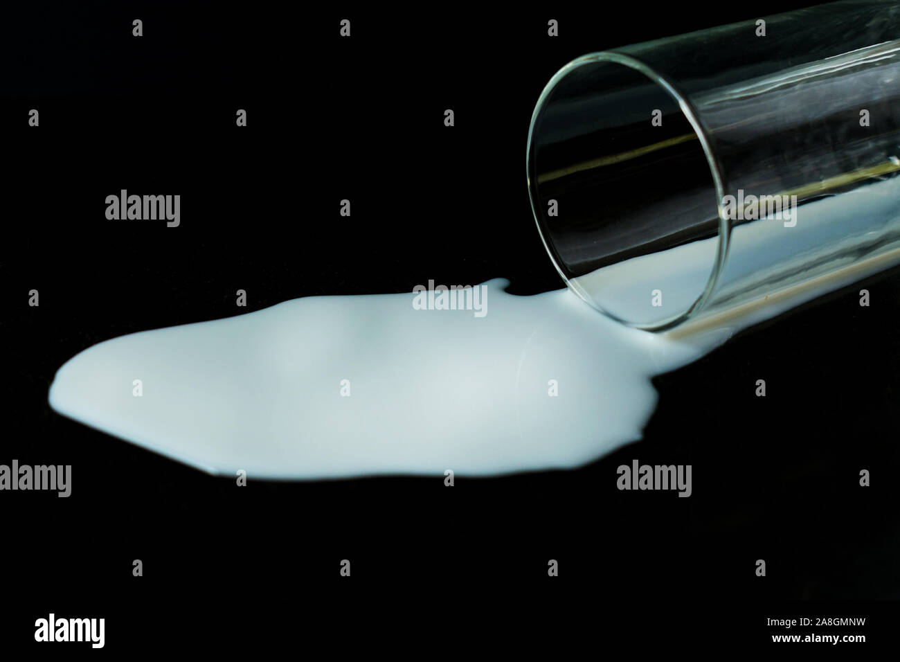 Un verre de lait renversé sur un fond noir. Banque D'Images Un verre de lait renversé sur un fond noir. Banque D'Images