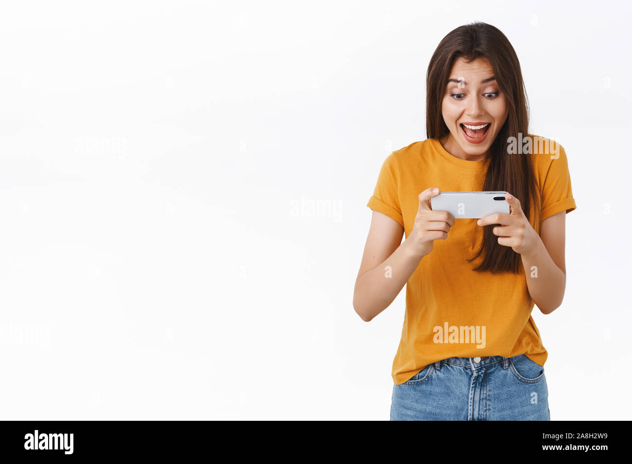 Heureux, joyeux de bon à la femme en t-shirt jaune jouer super amusant Nouveau jeu mobile, holding smartphone à l'horizontale, ils applaudissent, souriant et Banque D'Images