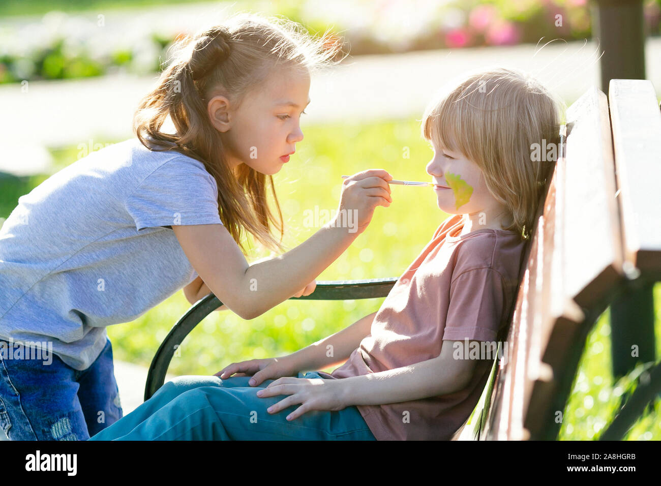 Une petite fille est l'application de maquillage aqua à la face d'un garçon  de 5 ans qui est assis sur un banc dans un parc Photo Stock - Alamy