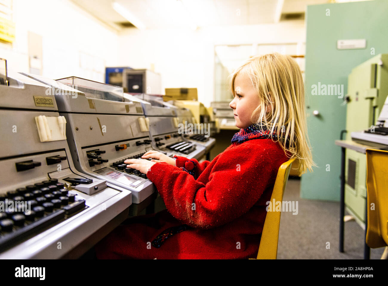 Une mignonne petite fille dans un manteau rouge est assis à un ordinateur à l'ancienne aérogare de Kelvedon Hatch nuclear bunker secret museum, des préparatifs de guerre, guerre froide Banque D'Images