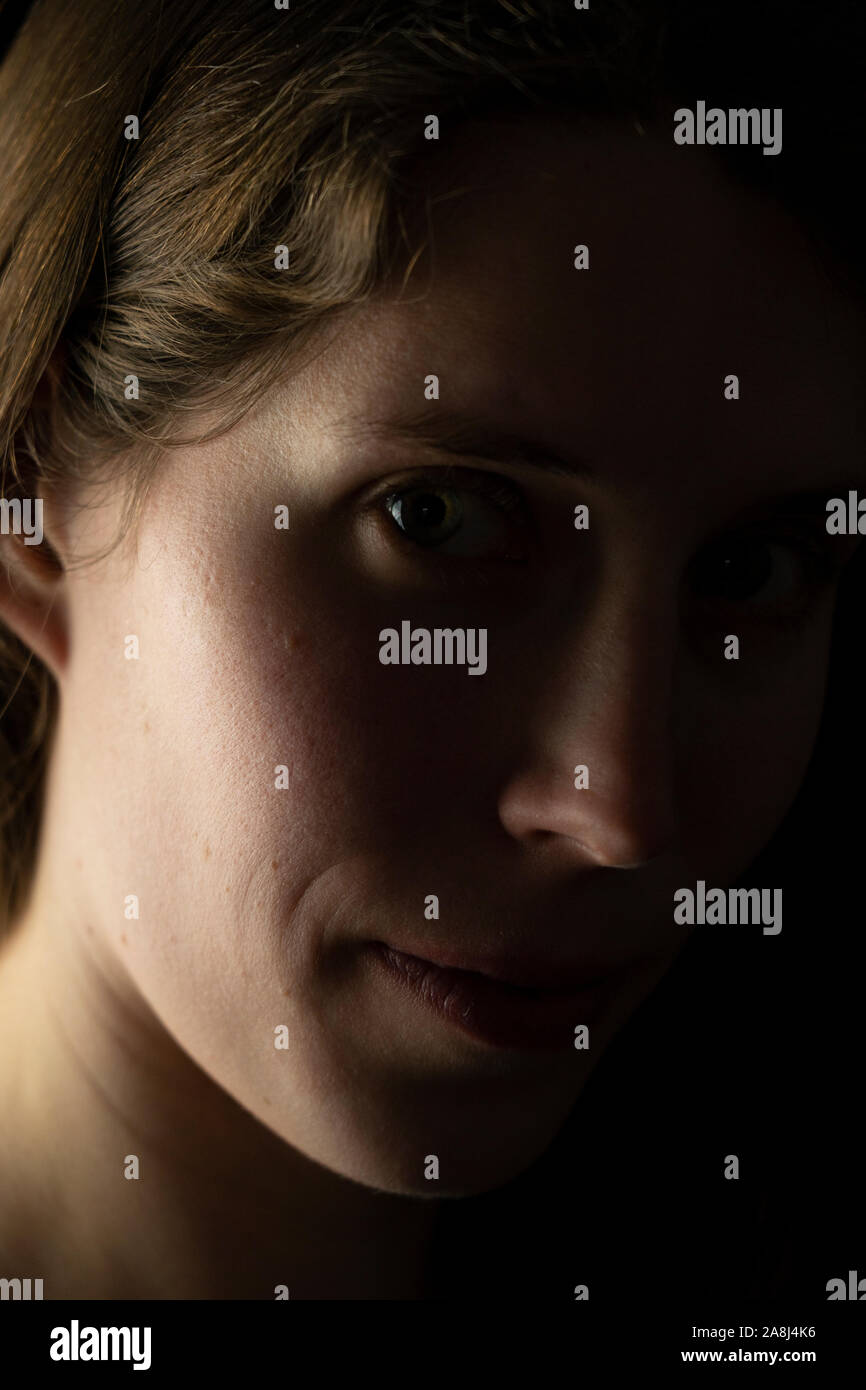 Un gros plan de profil d'un jeune visage de femme qui est de regarder directement le spectateur avec un demi-sourire et une expression mystérieuse Banque D'Images