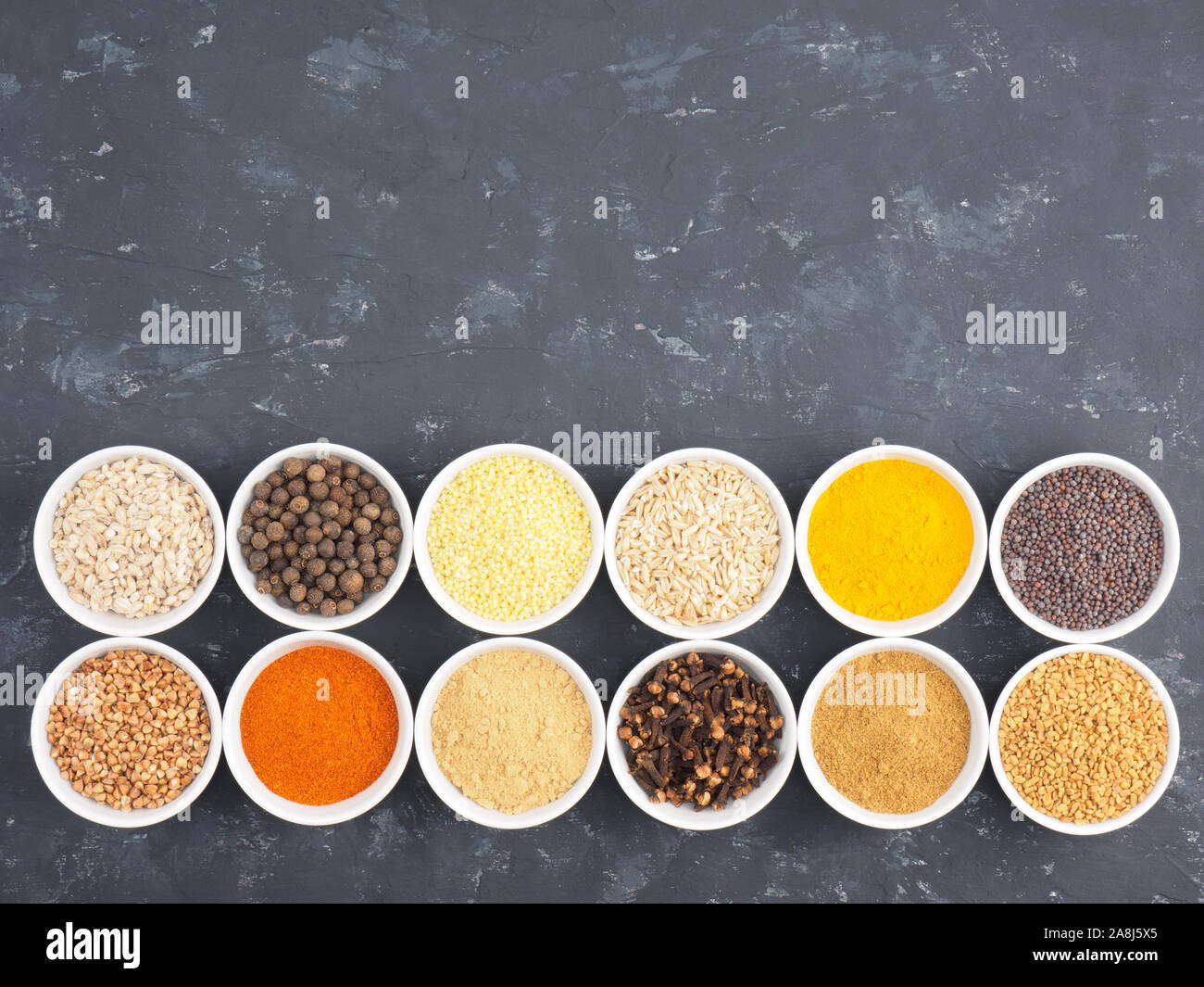 Le sarrasin, le millet, le piment, le fenouil, l'avoine, le poivre piment, masala, fenugrec, girofle, curcuma, cumin, graines de moutarde, la cardamome verte en blanc bols sur bl Banque D'Images