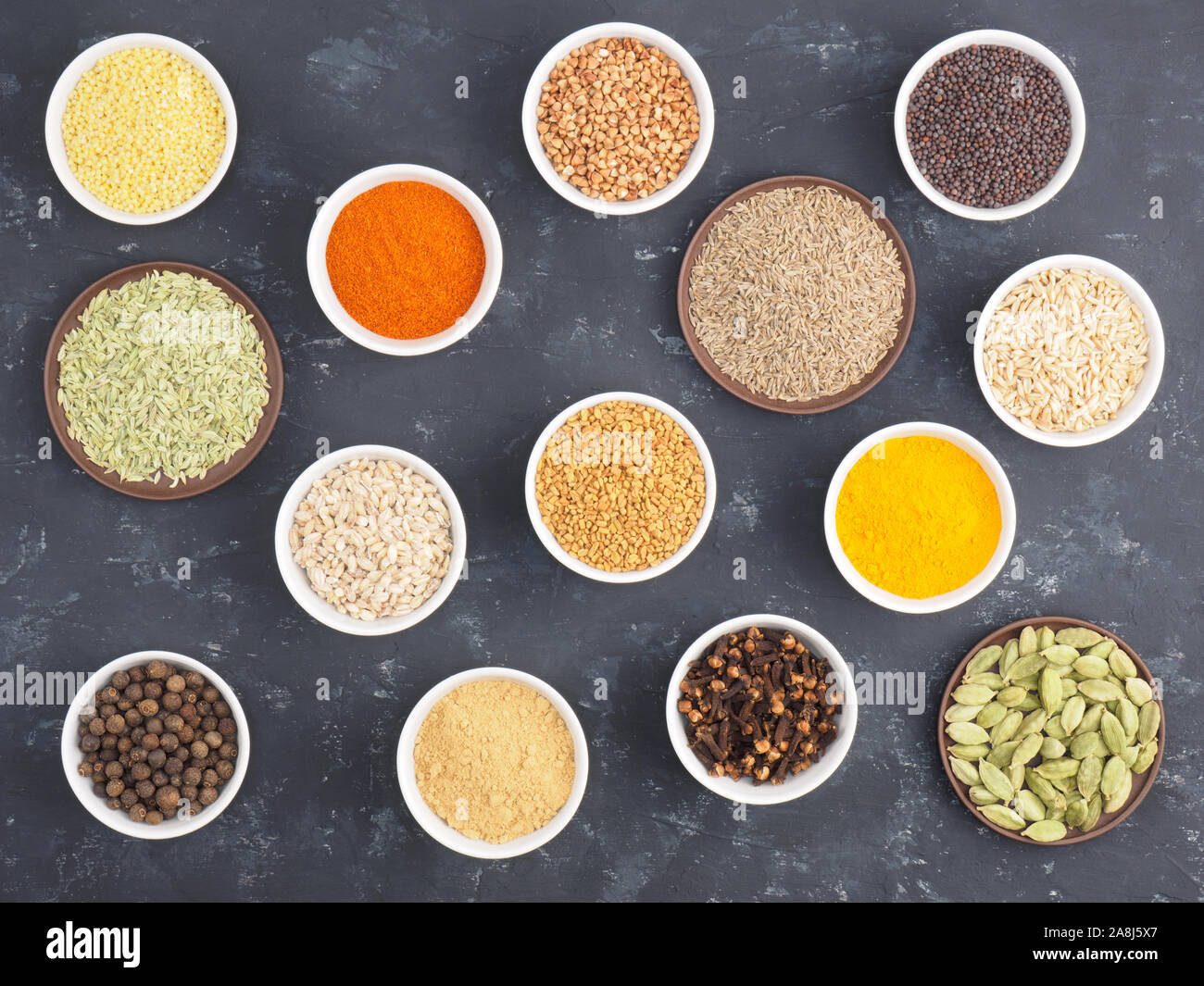 Le sarrasin, le millet, le piment, le fenouil, l'avoine, le poivre piment, masala, fenugrec, girofle, curcuma, cumin, graines de moutarde, de la cardamome verte sur béton noir ba Banque D'Images