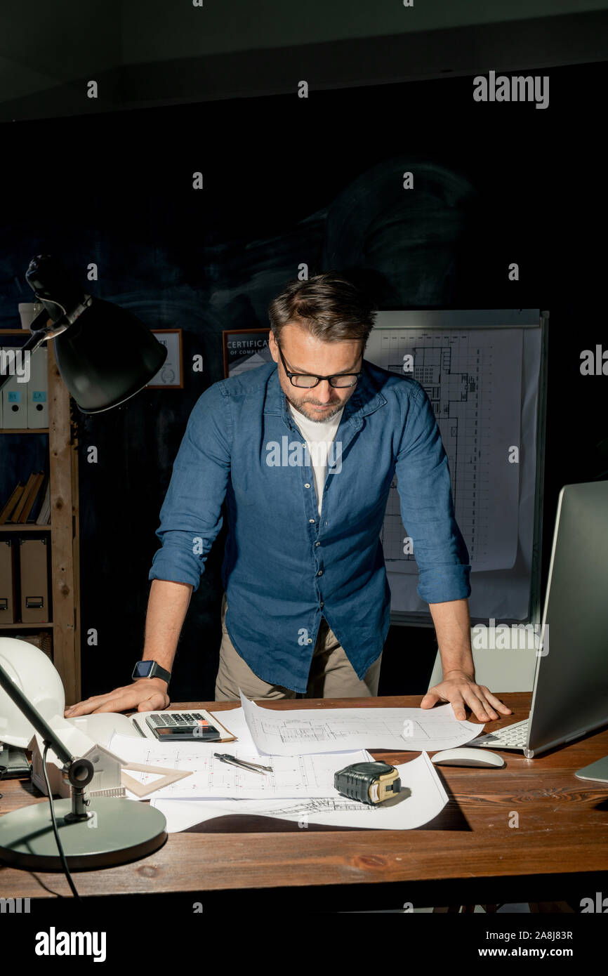 Ingénieur à la maturité à l'esquisse sur papier pendant les heures supplémentaires de nuit Banque D'Images