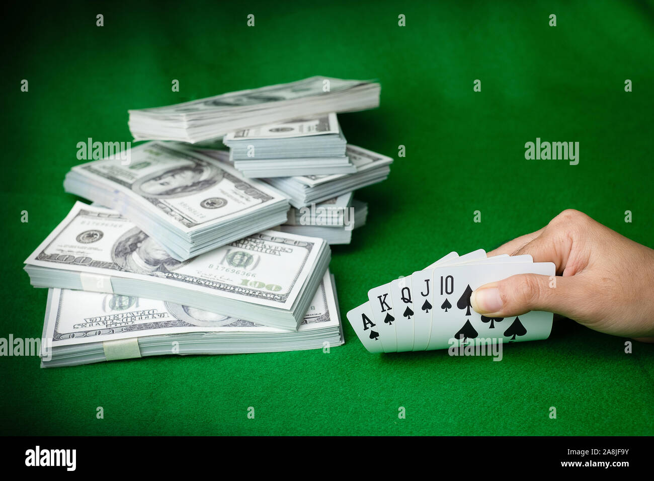 Les jeux de casino poker Quinte Flush Royale et l'argent pile de billets de 100 dollars US à l'arrière-plan vert, main tenant carte chat 5 Banque D'Images