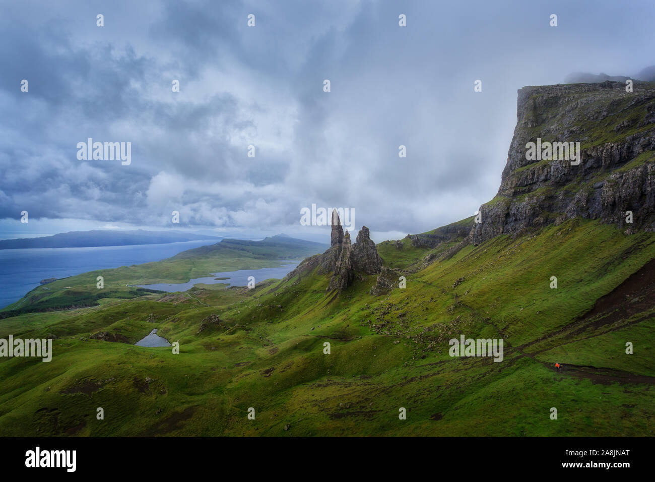 Old Man Storr. Le Storr sous un ciel nuageux dans un jour de pluie. Personne avec veste orange de la randonnée à travers l'herbe sous la pluie. Île de Skie, en Écosse. Banque D'Images