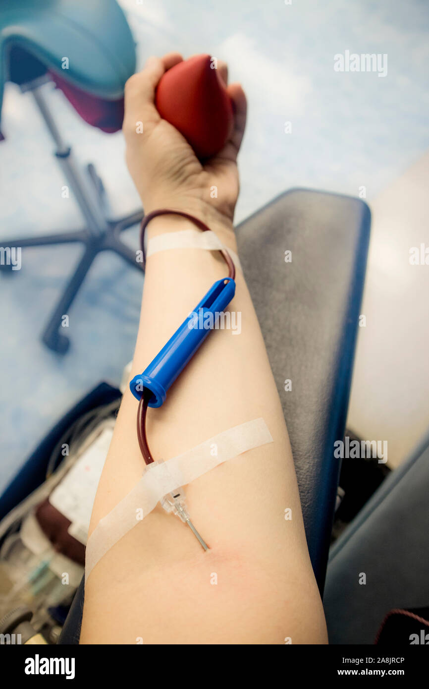 Selective focus sur la main du bras de femme avec aiguille à l'intérieur de la peau, le sang qui coule à travers le don d'équipement. Une femme heureuse le don de sang des donneurs c Banque D'Images