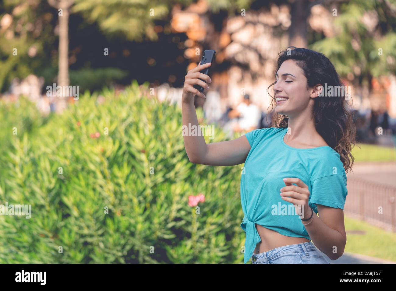 Smiling girl prenant un avec elle-même selfies derrière de plantes vertes Banque D'Images