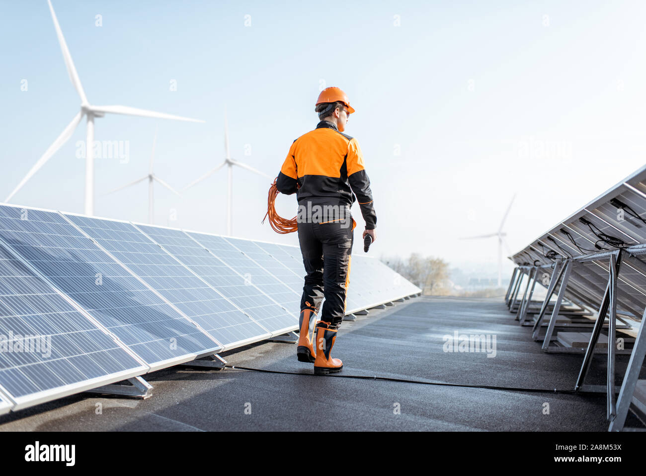 Travailleur bien équipé en vêtements orange de protection et d'examiner la marche des panneaux solaires sur un toit photovoltaïque usine. Concept de l'entretien et l'installation de stations solaires Banque D'Images