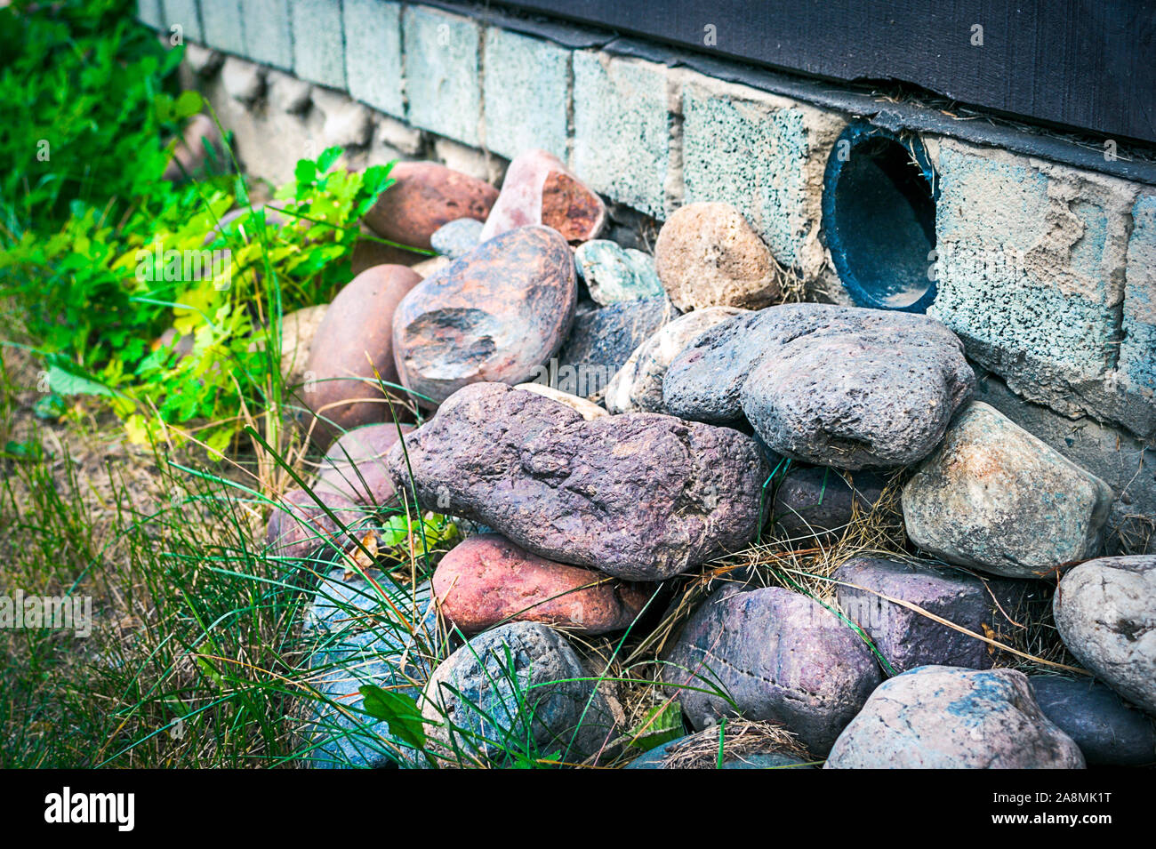 Amas de rochers colorés près d'une maison Fondation avec le tuyau en plastique pour assurer la circulation de l'air de ventilation sous le plancher et à prévenir la moisissure et la pourriture. Banque D'Images