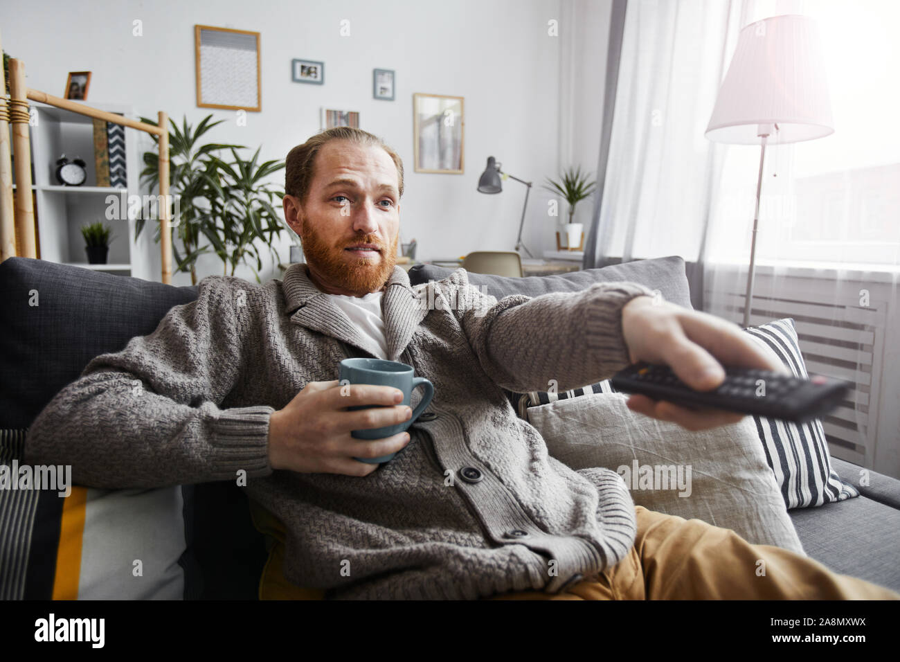 Portrait d'homme barbu d'âge moyen de regarder la télévision à la maison et de commutation satellite via la télécommande tout en vous relaxant sur le canapé confortable Banque D'Images