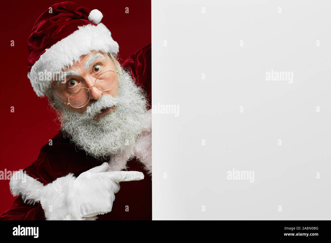 Portrait du Père Noël étonné looking at camera en pointant sur panneau blanc vierge, copy space Banque D'Images