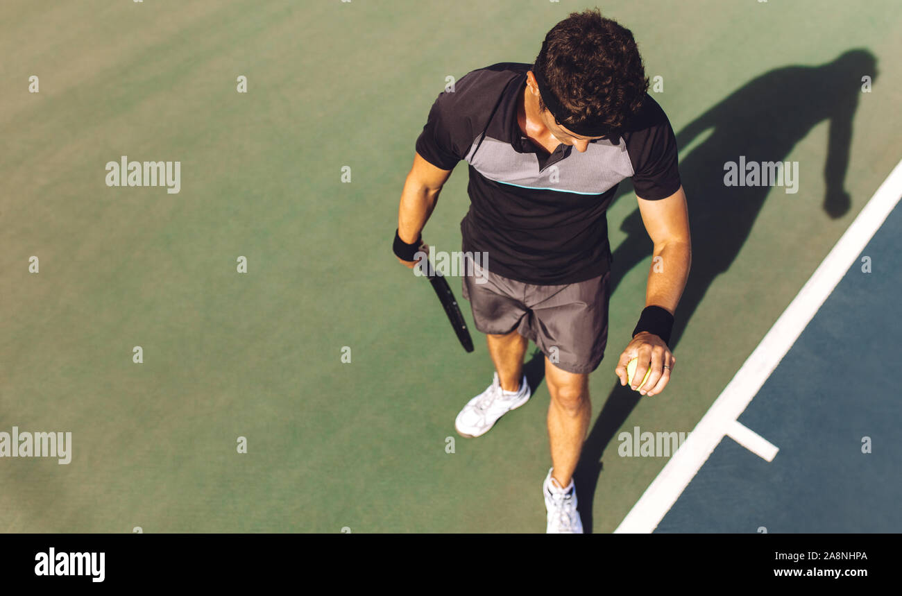 Vue de dessus du jeune homme jouant au tennis la balle qui rebondit sur le disque pour le servir. Tennis player a propos de servir le ballon dans un match. Banque D'Images