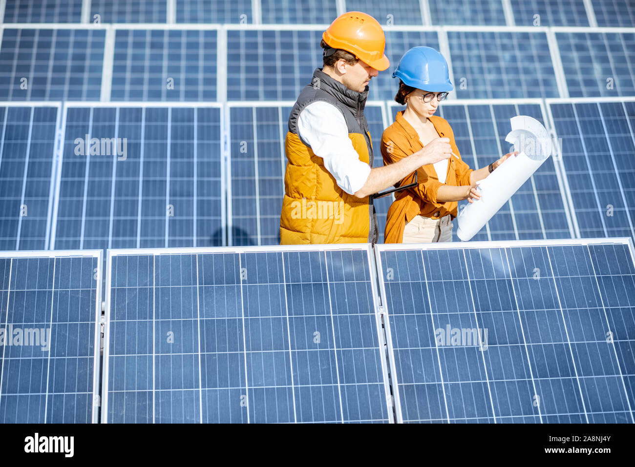 Deux ingénieurs ou d'architectes d'examiner la construction d'une centrale solaire, debout avec les bleus entre les rangées de panneaux solaires Banque D'Images