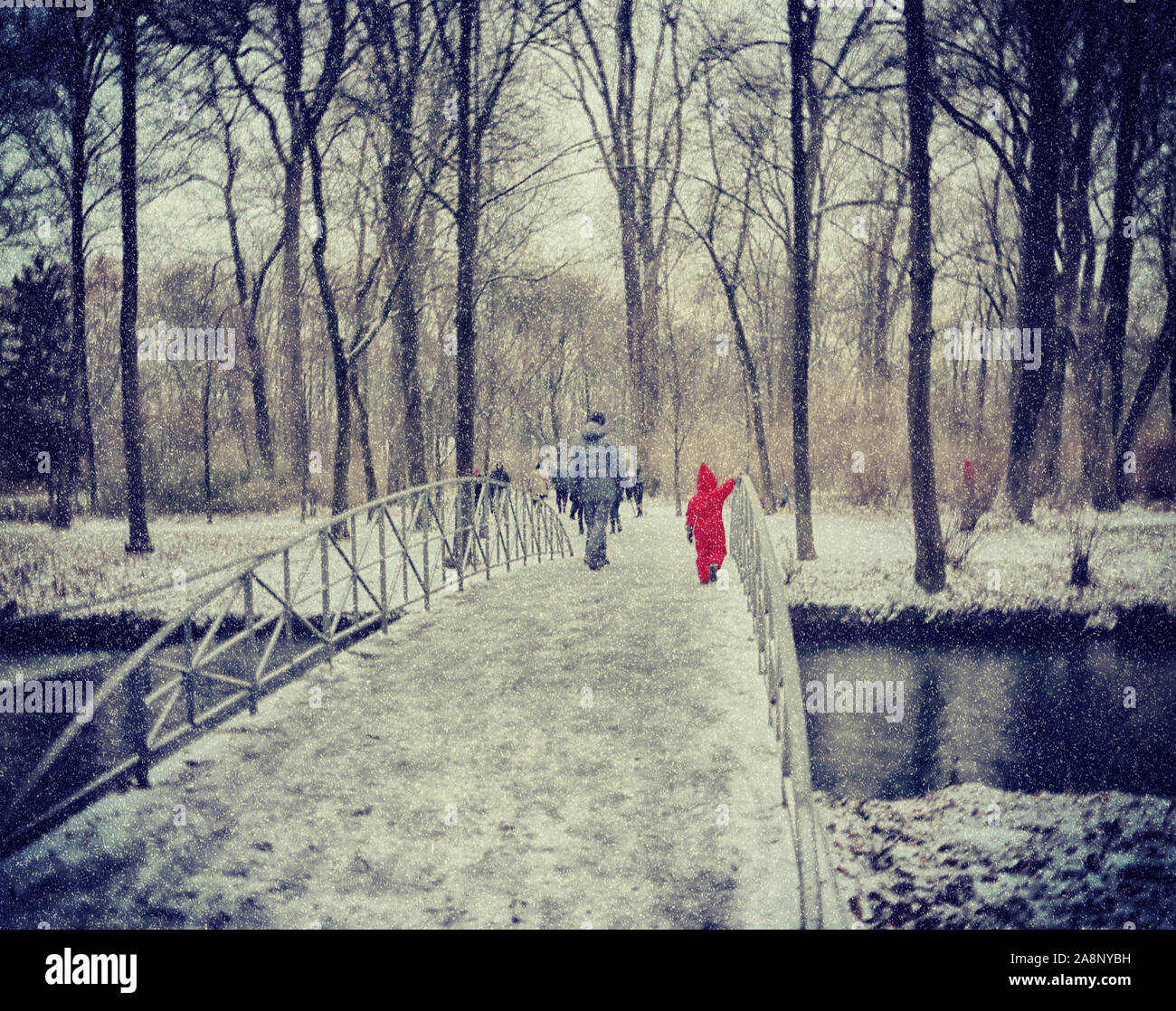 Décembre à Munich : bruine de neige à l'Englischer Garten, personnes et un enfant avec combinaison de saut rouge faire une promenade dans le parc Banque D'Images
