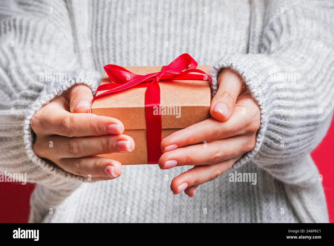 Female hands holding gift box with red ribbon close-up. Banque D'Images