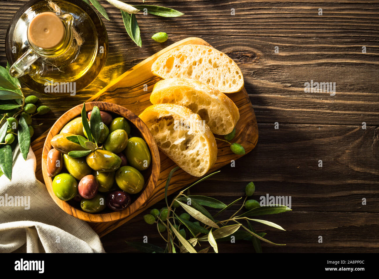 Olives, huile d'olive et pain ciabatta sur table en bois. Banque D'Images