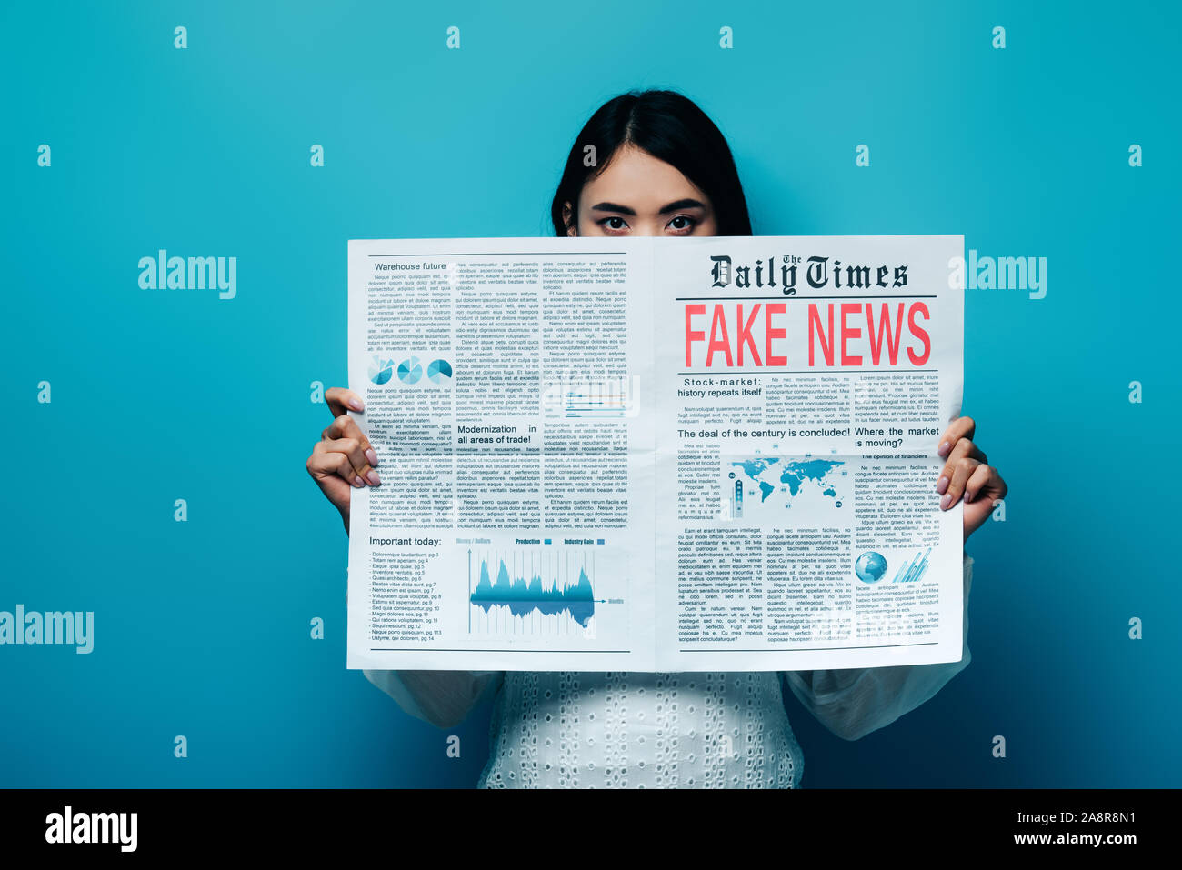 Femme asiatique en blouse blanche tenant un journal avec de fausses nouvelles sur fond bleu Banque D'Images