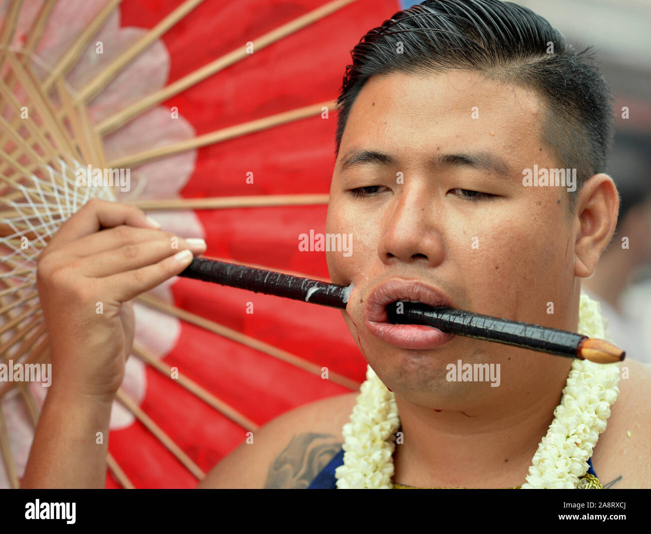 Séduit les jeunes Chinois thaïlandais dévot taoïste (mah) Chanson perce sa joue droite avec un parasol en bois au cours de la poignée Festival Végétarien de Phuket. Banque D'Images