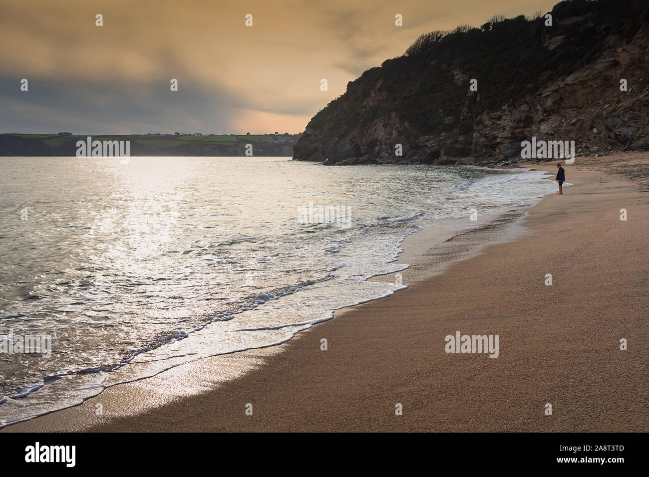 Un garçon regardant la mer sur une plage, à Cornwall, en Angleterre. Le soir, coucher de soleil magnifique en arrière-plan. Banque D'Images