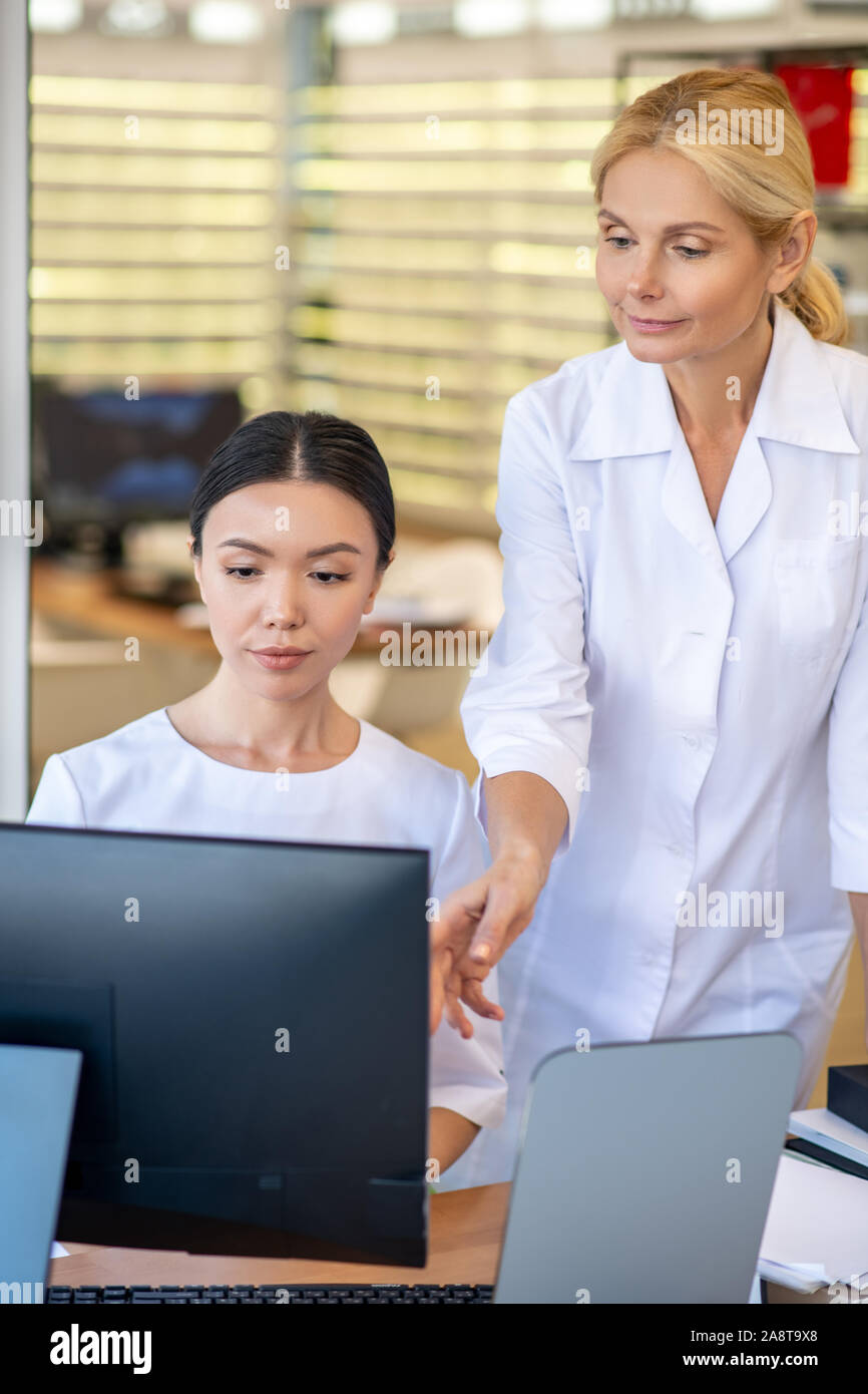 Dark-haired stagiaire du médecin assis à l'ordinateur pendant le processus d'apprentissage Banque D'Images