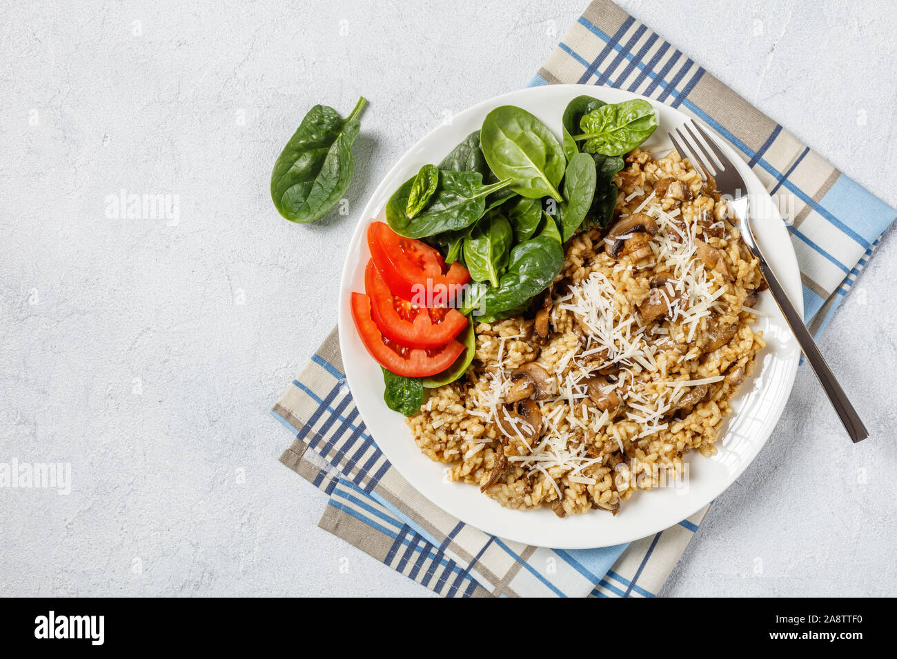 Champignons sauvages risotto crémeux aux épinards et fromage râpé salade de tomates sur une assiette blanche, vue horizontale à partir de ci-dessus. flatlay, espace libre Banque D'Images