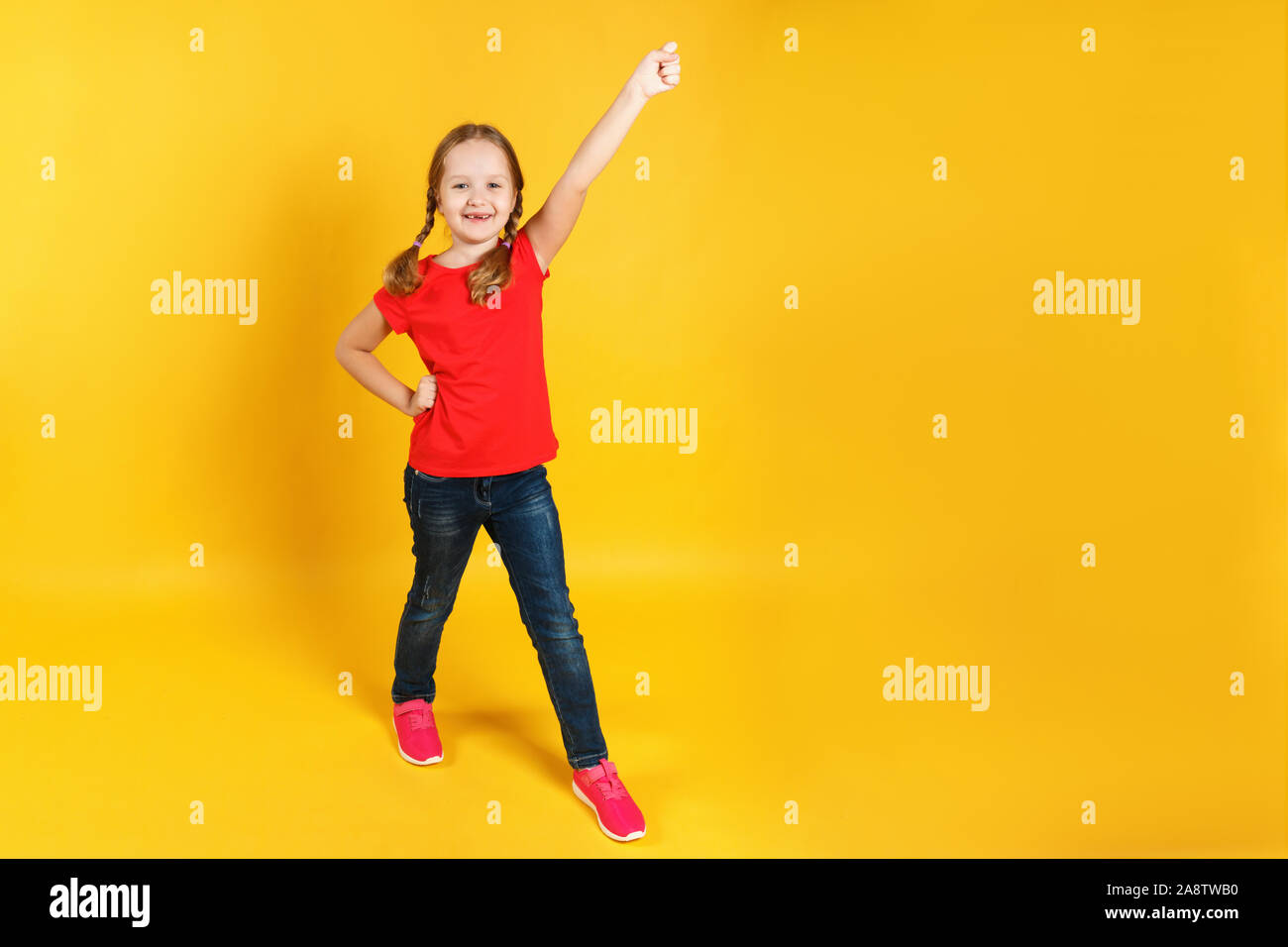 L'enfant est pleine longueur et leva la main. Petite fille joyeuse dans les jeans et un T-shirt rouge sur fond jaune. Banque D'Images