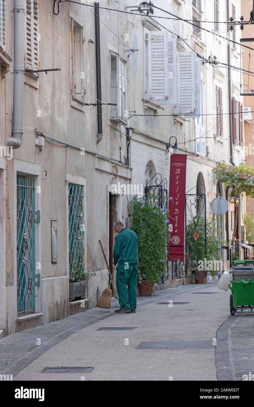 Un travailleur d'âge moyen de l'assainissement balaye une charmante vieille fashion street près de la place Tartini à Piran, Slovénie. Banque D'Images