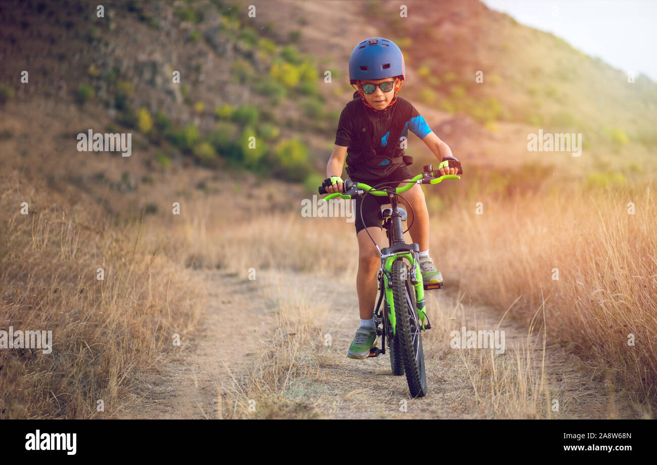 Happy kid garçon de 7 ans s'amuser dans le parc de l'automne avec un vélo sur belle journée d'automne. Casque de vélo enfant portant Active Banque D'Images