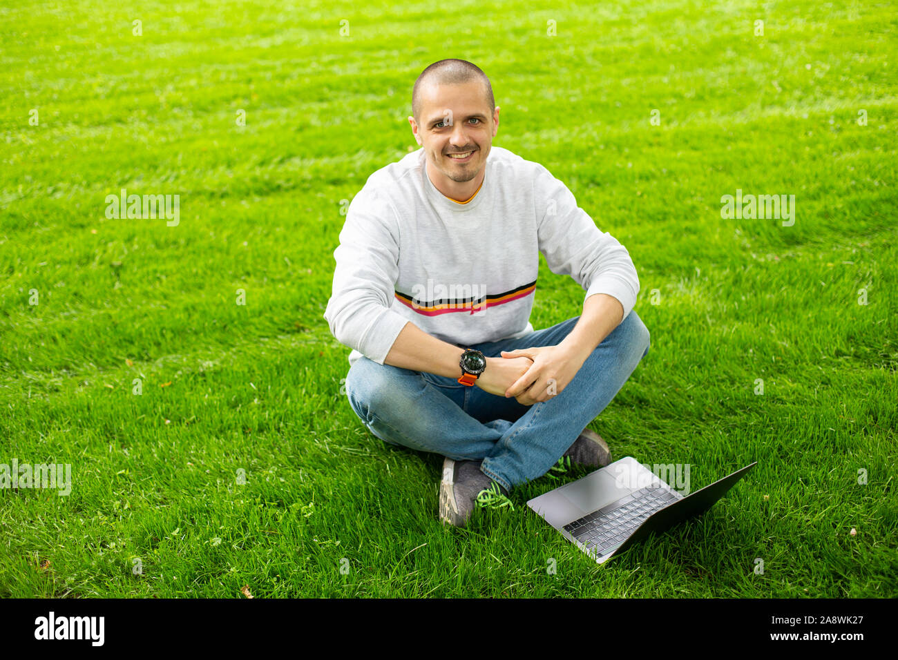 Smiling Man lookin à huis clos et assis sur pelouse verte avec portable Banque D'Images
