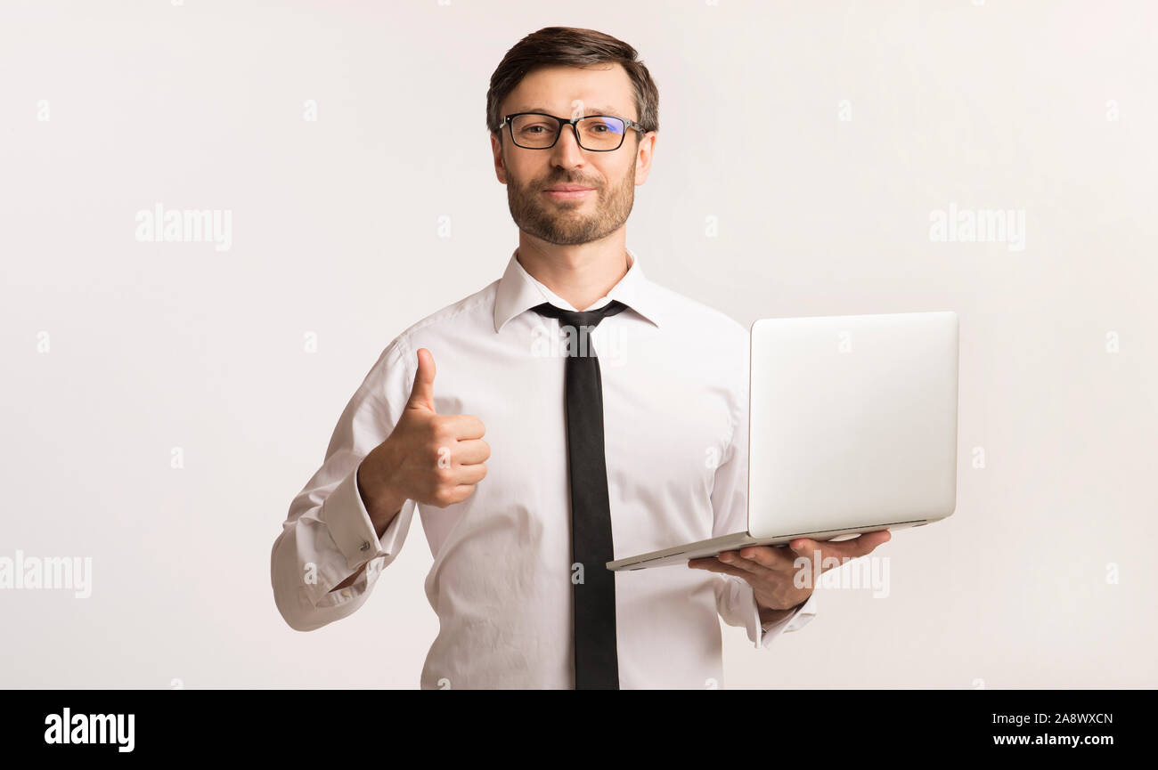 Confident Businessman Holding Laptop Gesturing Thumbs-Up, Studio Shot Banque D'Images