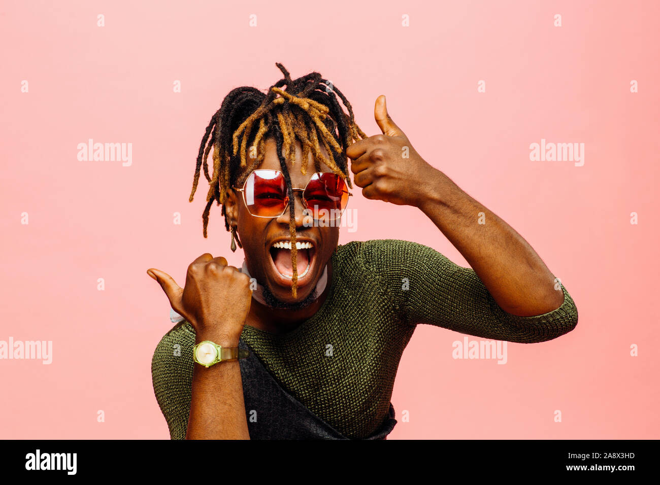 Portrait d'un jeune homme gai avec bouche ouverte laughing with Thumbs up, isolé sur Rose Banque D'Images