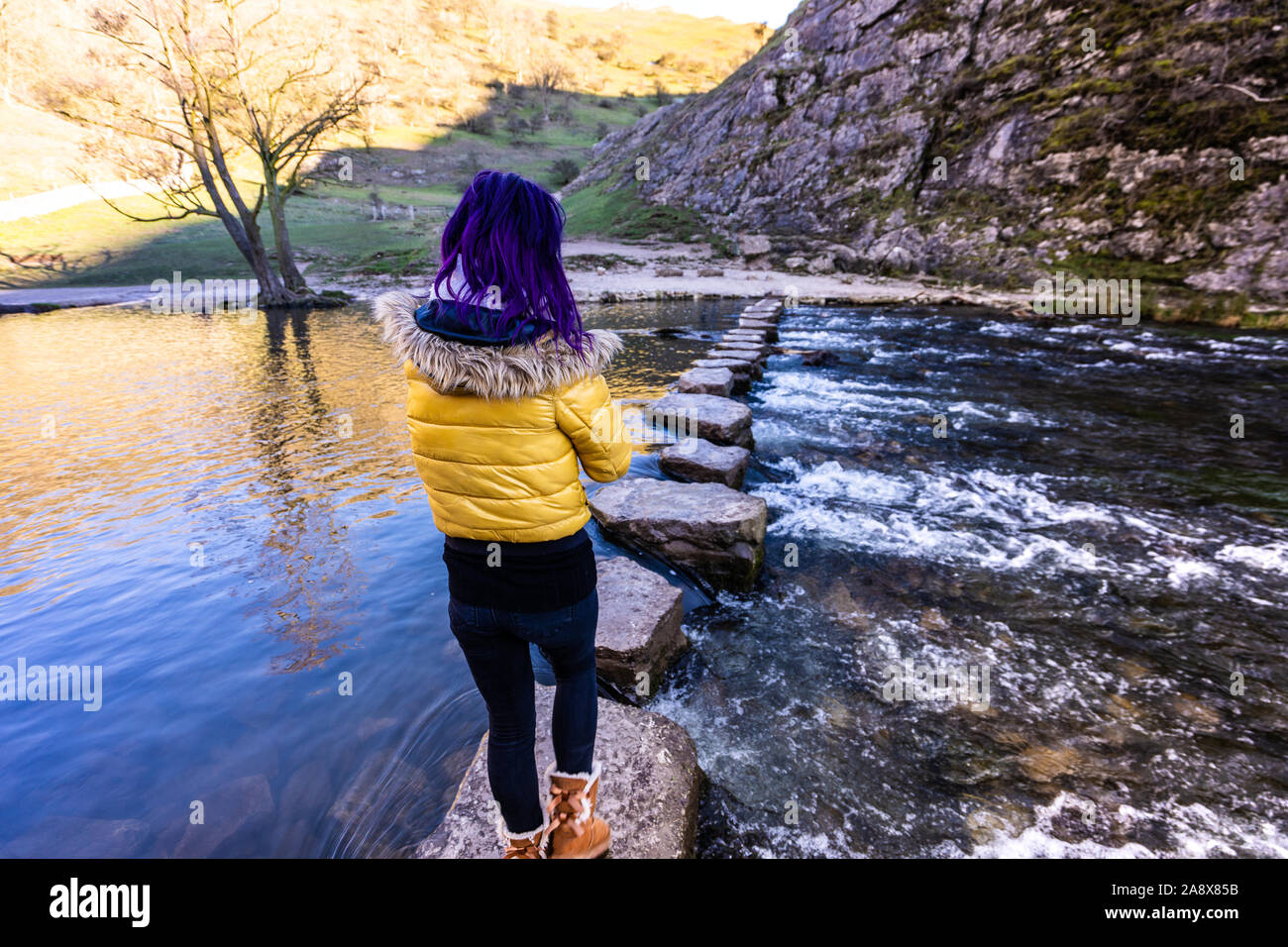 Une jolie jeune femme athlétique passe au-dessus de la célèbre Dovedale stepping stones, garder son équilibre sur les roches glacées, National Trust, Peak District Banque D'Images