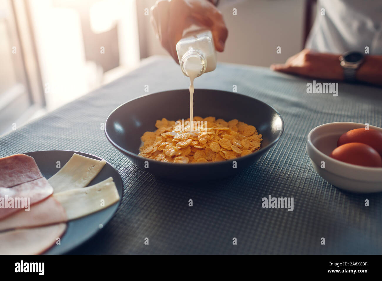 Cornflake avec du lait petit-déjeuner. Man pouring en bouteille Verre de lait dans un bol avec des céréales sèches. Banque D'Images