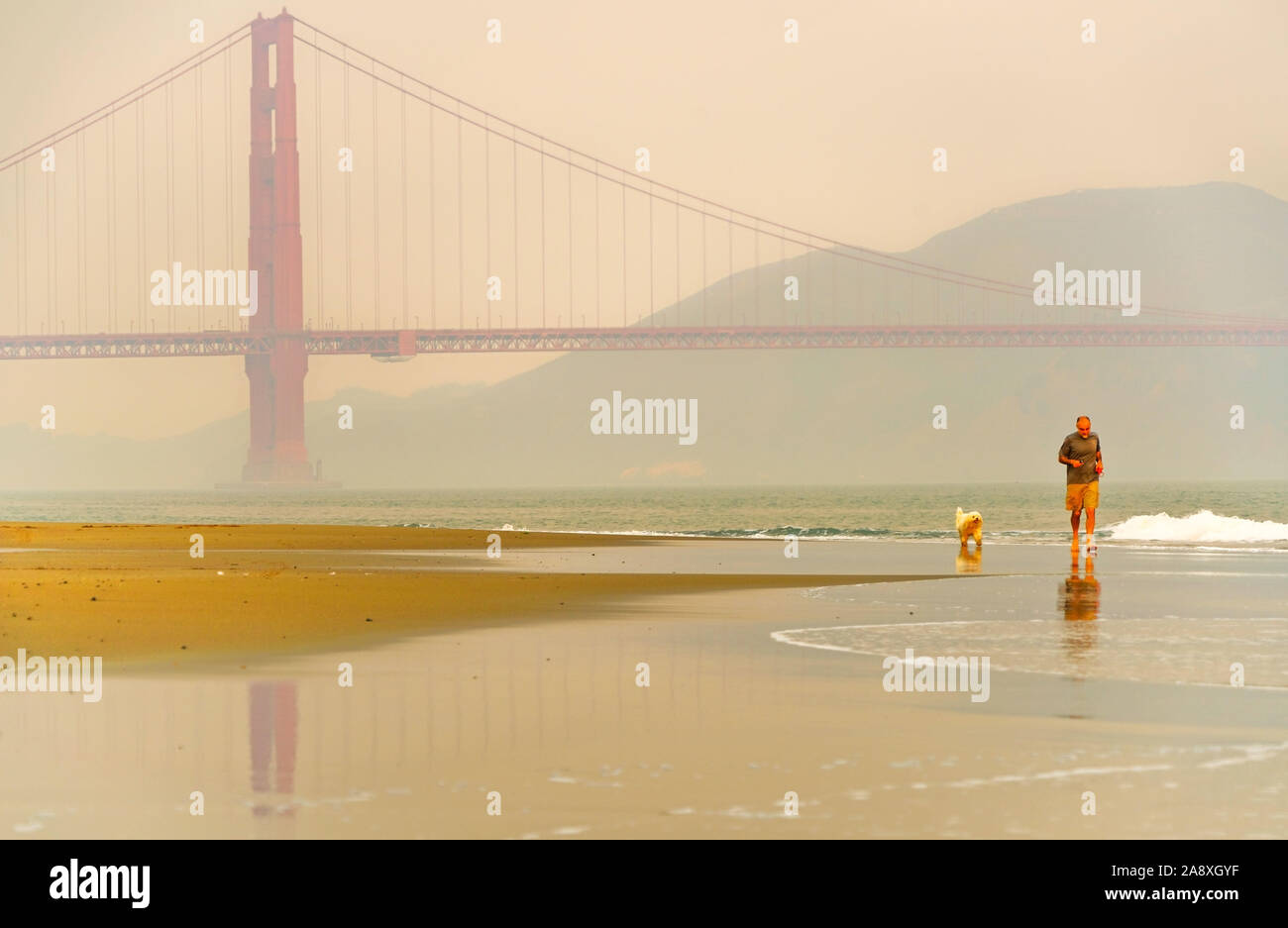 Vue sur le Golden Gate Bridge avec des gens et son chien de jogging le long de la plage est à San Francisco au lever du soleil. Banque D'Images