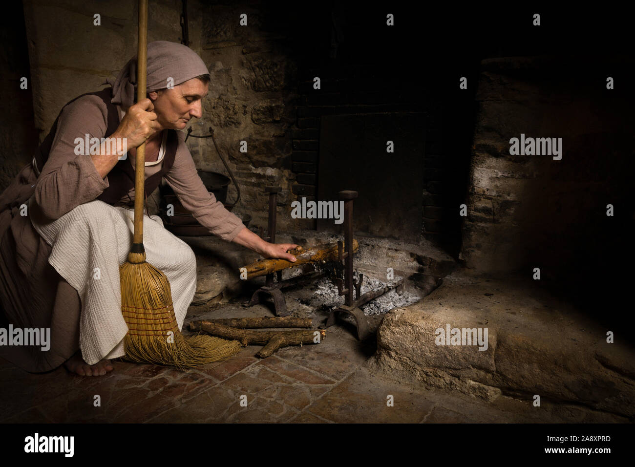 Femme en costume de femme de la renaissance le bois de sciage pour l'ajout d'un feu brûlant dans la cuisine d'un château médiéval authentique, libéré de la propriété en France Banque D'Images