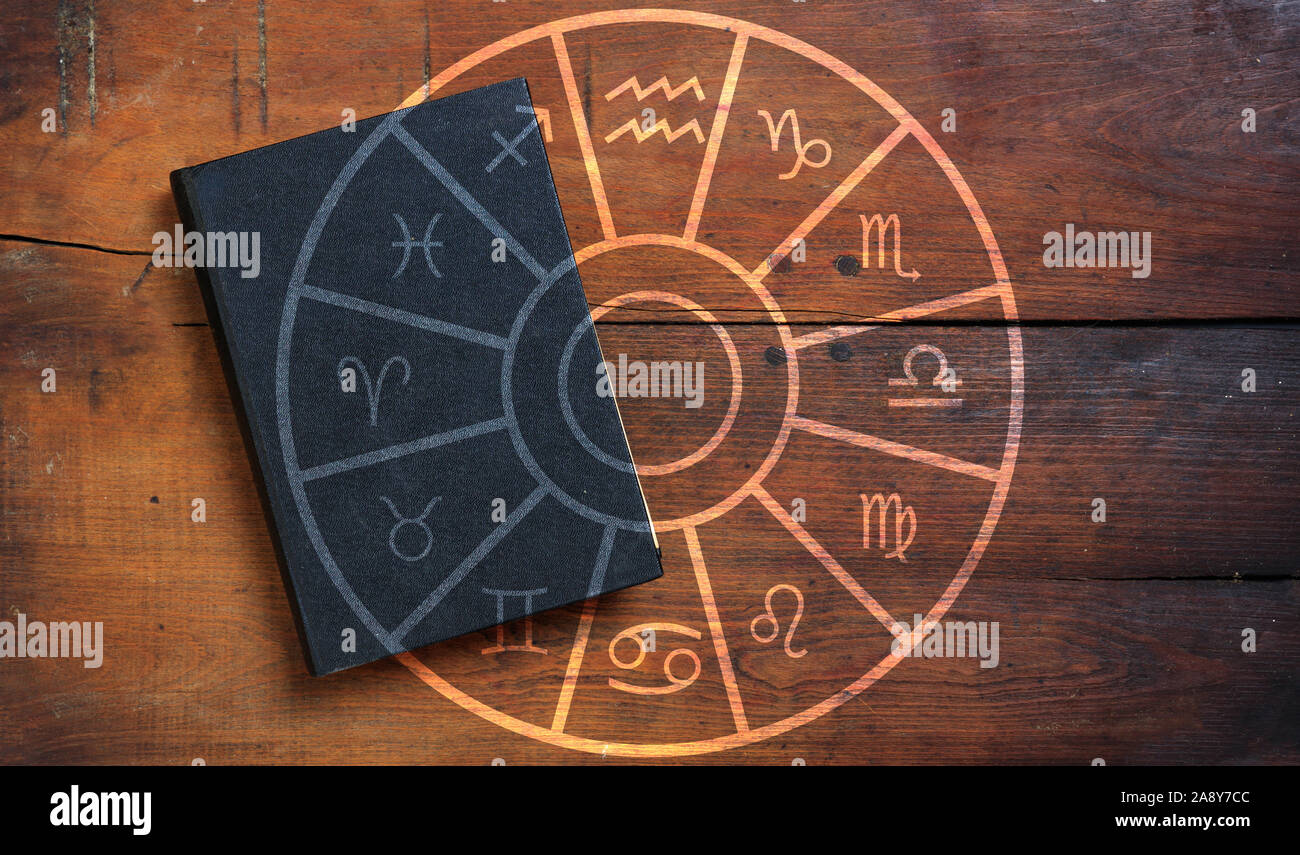 L'astrologie et les horoscopes concept. Livre noir et signes du zodiaque astrologique roue sur fond de bois. Banque D'Images