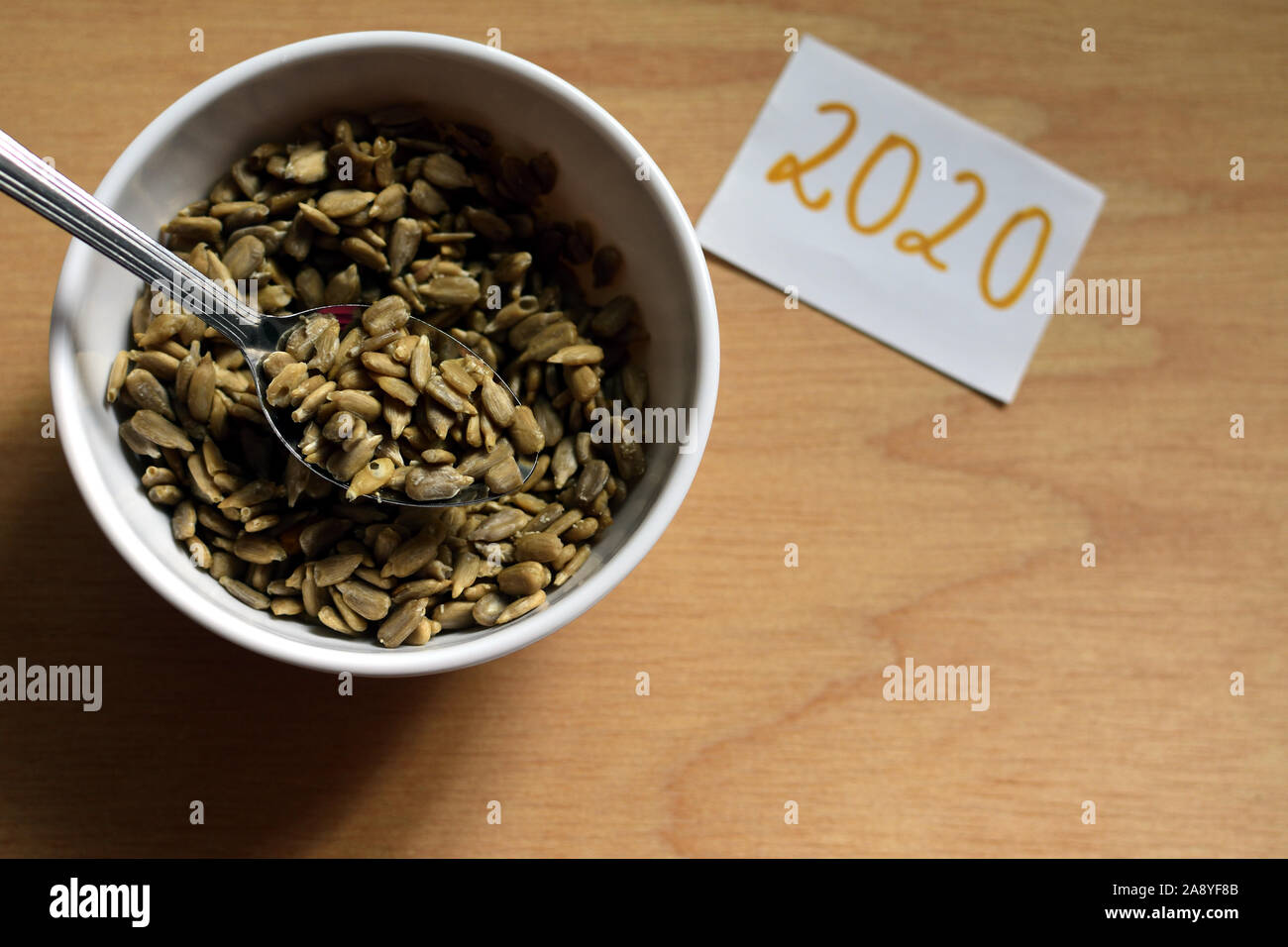 Graines de tournesol en blanc bol avec cuillère sur fond de bois et le numéro 2020 d'en haut Banque D'Images