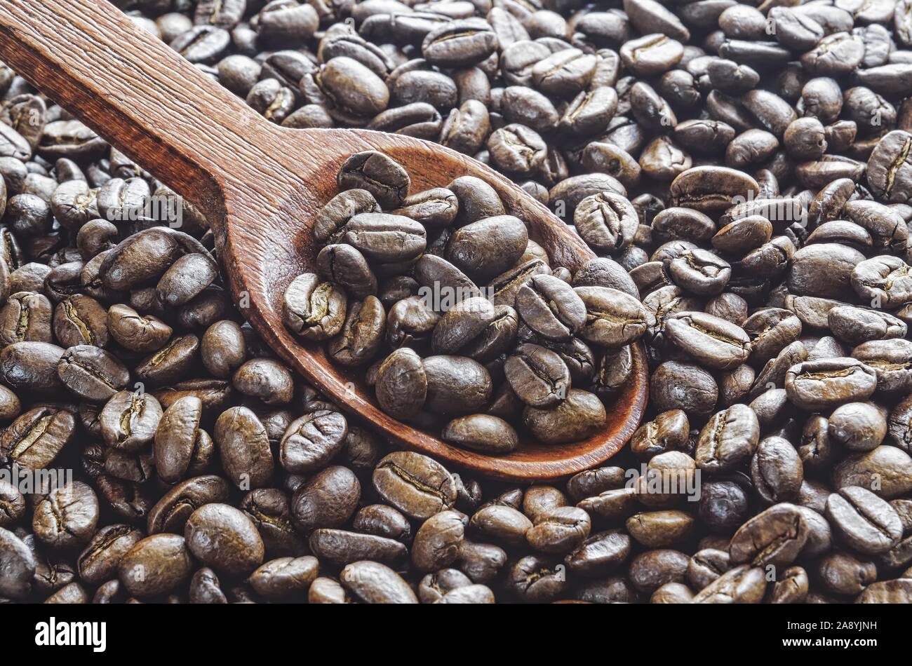 Café noir foncé. Des grains de café frais avec une cuillère en bois. Banque D'Images