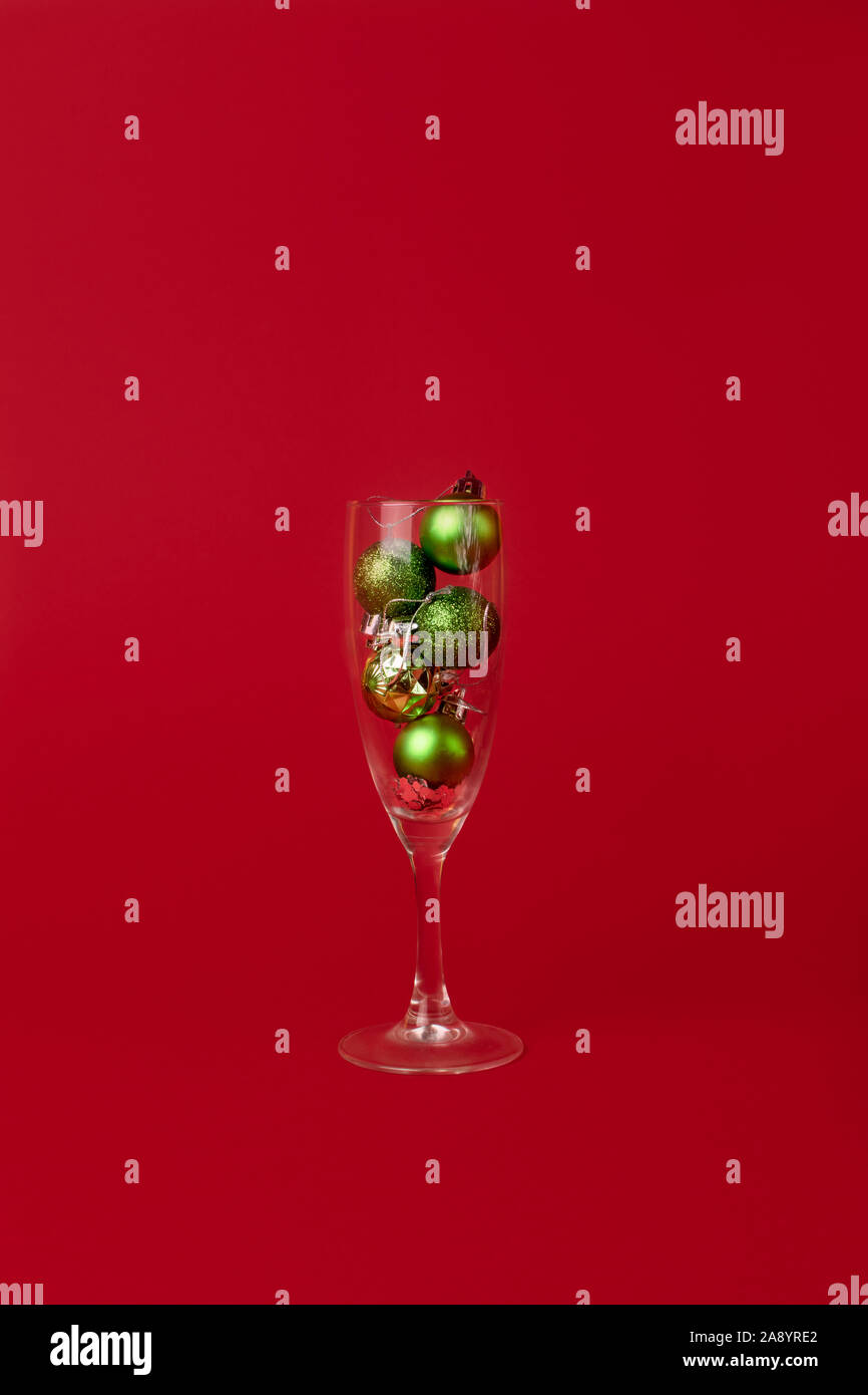 Peu de vert des boules de Noël est à l'intérieur d'un verre de champagne sur un fond rouge. Un style minimaliste. Banque D'Images