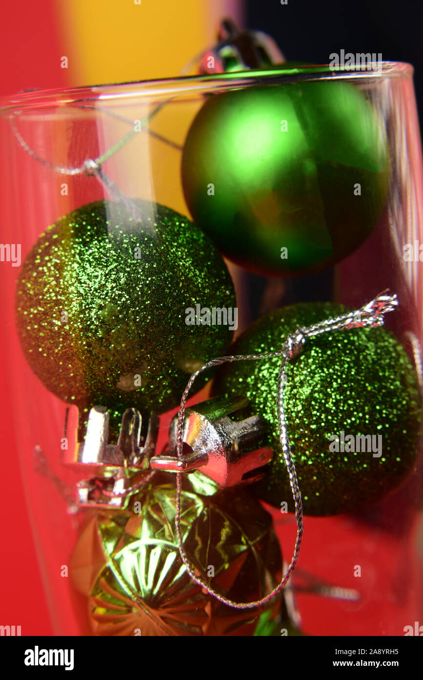 Les petites boules de Noël vert est à l'intérieur d'un verre de champagne sur un fond jaune-rouge. Close-up Banque D'Images