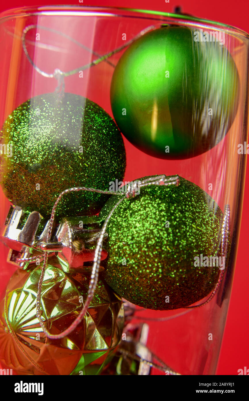 Peu de vert des boules de Noël est à l'intérieur d'un verre de champagne sur un fond rouge. Close-up. Banque D'Images