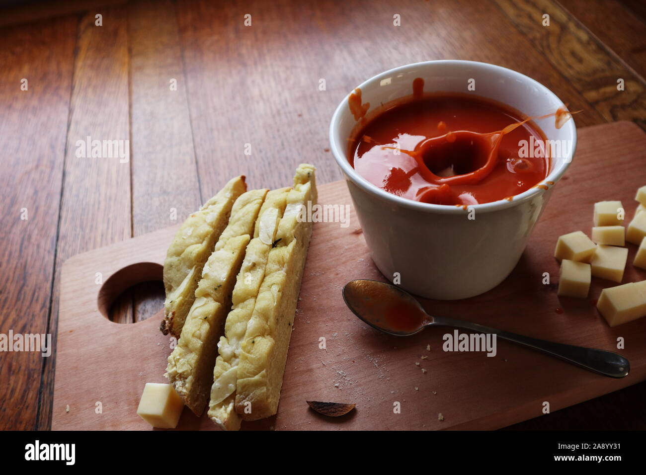 Cubes de fromage de tomber dans la soupe aux tomates dans un bol blanc et faire un splash avec plus de cubes de fromage sur le côté et de tranches de pain focaccia Banque D'Images