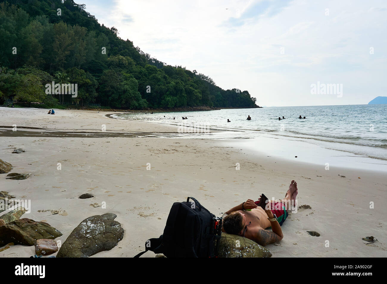 Langkawi, Malaisie - le 12 octobre 2019. Guy jeter sur plage de Pasir Tengkorak et regarder sur son téléphone. Banque D'Images