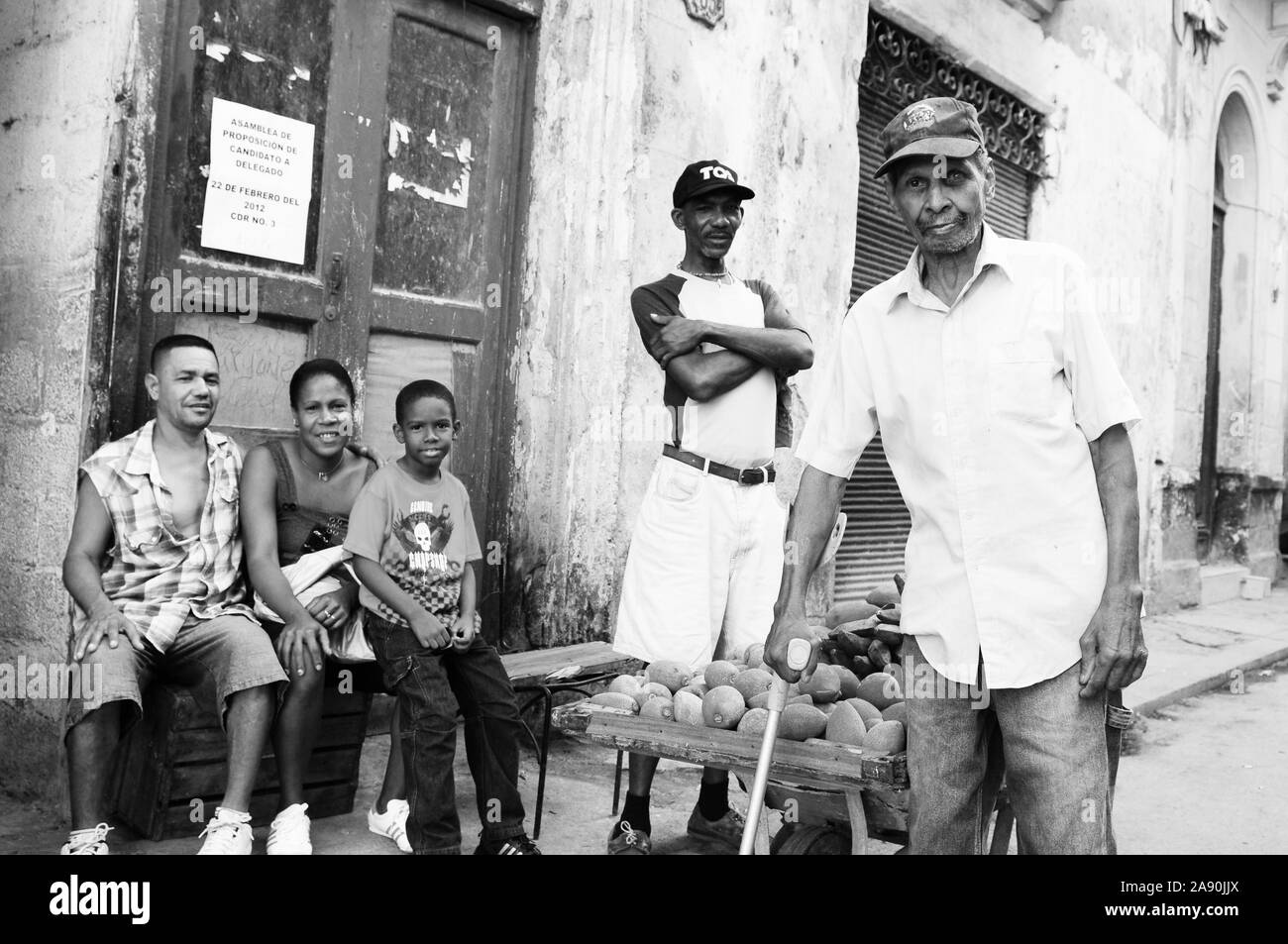 La Havane : peuple cubain assis sur la rue offrant des fruits, alors qu'un vieil homme marche Banque D'Images